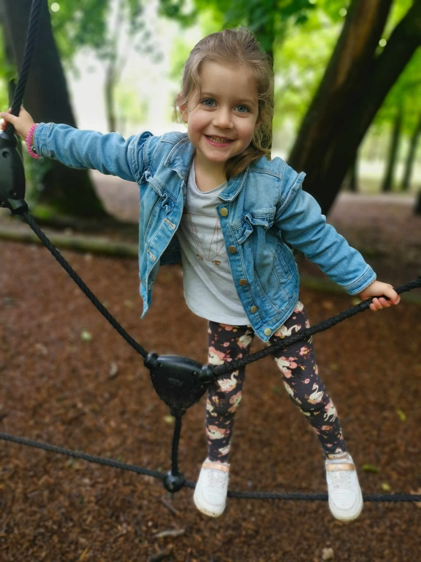 Emma participe au concours pour gagner de l'argent avec cette photo : child, girl, smiling, denim_jacket, leggings, white_shoes, rope, playground, outdoor, forest, tree, nature, happy, casual_clothing, young, fun, active, daylight, portrait, cute