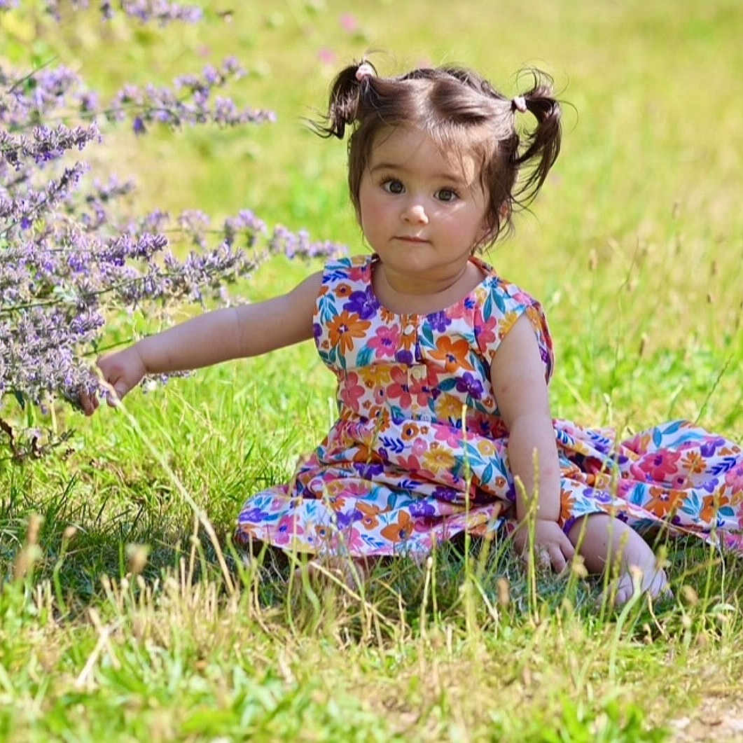 Stella a rejoint le concours — aidez-le/la à gagner de superbes lots ! bush, child, curious, cute, dress, floral_pattern, flower, girl, grass, greenery, innocence, nature, outdoor, pigtails, portrait, sitting, summer, sunlight, toddler, young_child
