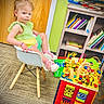 Gracelynn is registered to the contest to win money with this photo: activity_toy, books, bookshelf, carpet, chair, child, colorful_clothing, curious, expression, floor, furniture, indoor, person, pink_shoes, playroom, seated, toddler, toy, wooden_door, wooden_legs