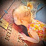 bright_colors, child, close_up, curly_hair, daylight, engravings, exploring, face, floral_dress, girl, hand, outdoor, person, plaque, pony_tail, portrait, stone, sunlight, texture, toddler