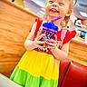 Gracelynn joined the competition — help win amazing prizes! blond_hair, casual, child, clothing, colorful_dress, cup, girl, happy, indoor, joyful, person, playful, portrait, red_cushion, restaurant, smiling, straw, table, wood_paneling, young_child