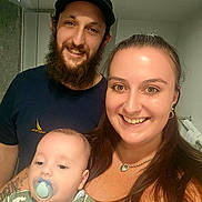 Austin is registered to the contest to win money with this photo: family, baby, man, woman, smile, pacifier, beard, cap, tattoo, necklace, indoor, bathroom, mirror, towel, clothing, portrait, people, happy, child, dinosaur_print