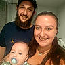 family, baby, man, woman, smile, pacifier, beard, cap, tattoo, necklace, indoor, bathroom, mirror, towel, clothing, portrait, people, happy, child, dinosaur_print