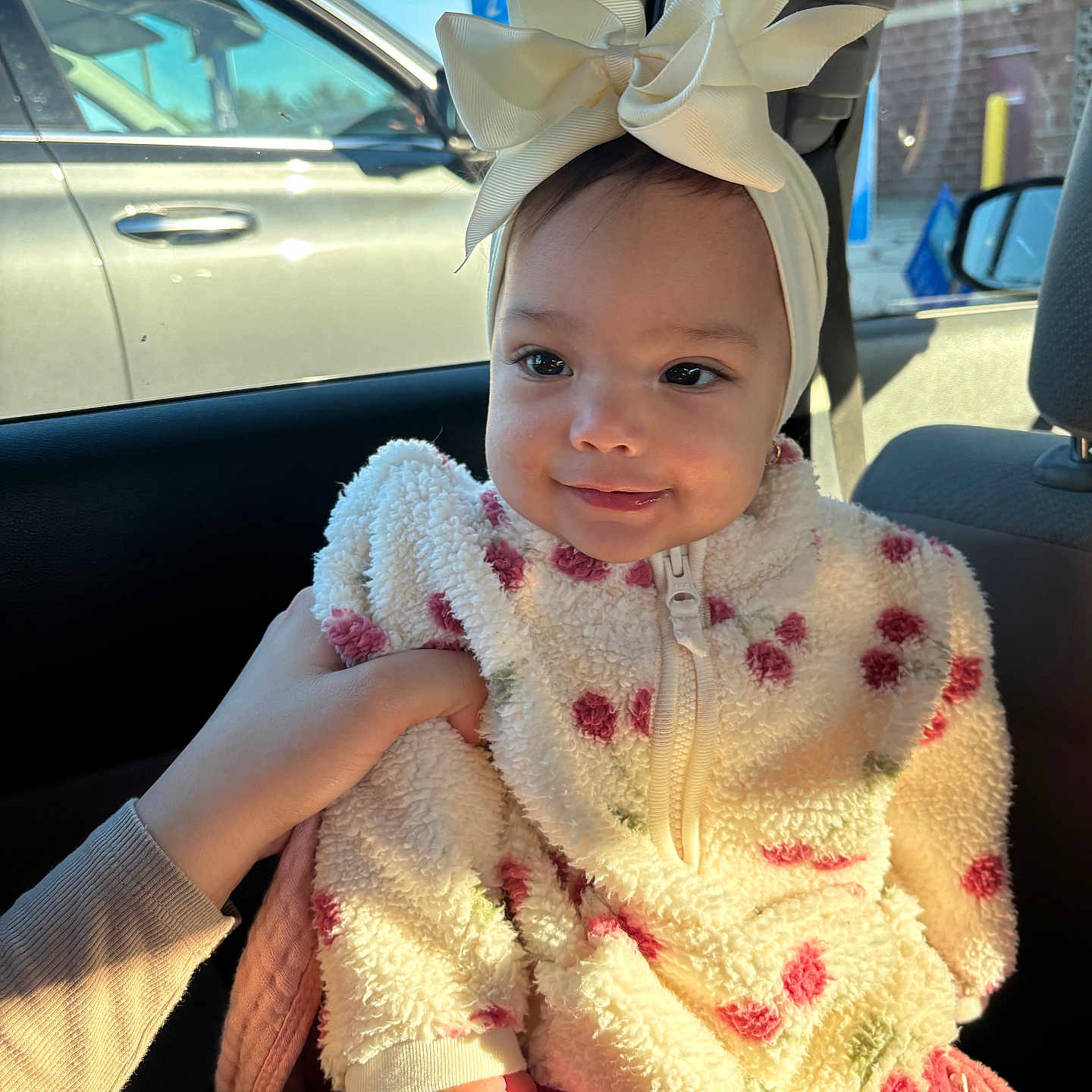 Arleth joined the competition — help win amazing prizes! baby, bow, car, car_interior, child, clothing, cute, face, floral_pattern, hand, headband, infant, jacket, person, pink_pants, portrait, seat, smile, sunlight, window