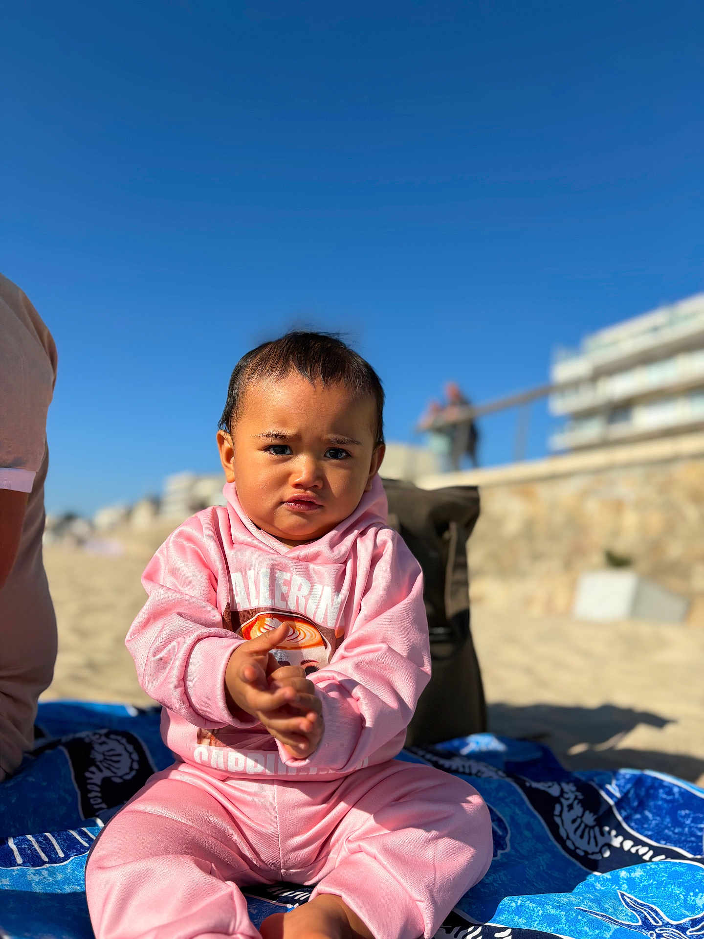 Isalei a rejoint le concours — aidez-le/la à gagner de superbes lots ! child, toddler, pink_clothing, beach, sand, blue_sky, sunny, towel, outdoor, portrait, casual, young_child, person, sitting, daylight, serious_expression, clothing, vacation, holiday, playful