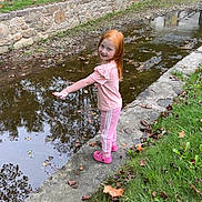 Brooklynn is registered to the contest to win money with this photo: child, girl, red_hair, pink_clothing, water, canal, stone_wall, grass, leaves, autumn, outdoor, playful, smiling, park, reflection, trees, sidewalk, casual, nature, daytime