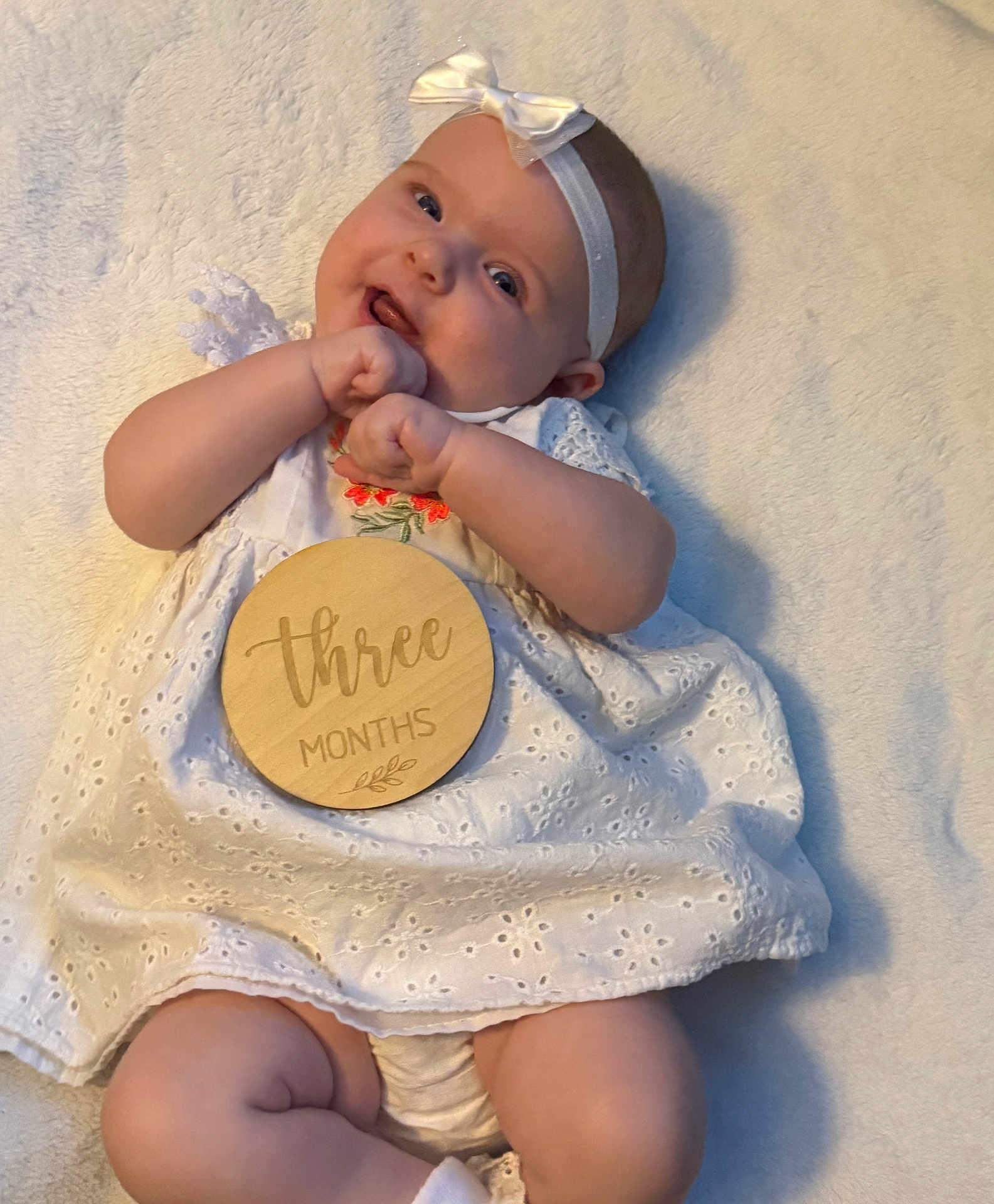 Rynleigh joined the competition — help win amazing prizes! baby, infant, child, white_dress, headband, bow, smile, happy, lying_down, blanket, soft_texture, wooden_plaque, three_months, cute, chubby, hands, legs, closeup, portrait, indoors
