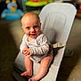 baby, infant, child, smiling, sitting, baby_rocker, clothing, onesie, indoors, carpet, toy, colorful, face, happy, cute, hands, foot, head, person, portrait