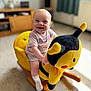 Nathan is registered to the contest to win money with this photo: baby, child, smiling, rocking_toy, plush_toy, bee_toy, indoor, carpet, wooden_furniture, living_room, happy, cute, toddler, shorts, socks, toy, play, person, seat, fun