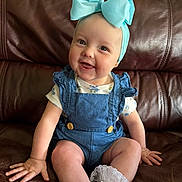 Emery is registered to the contest to win money with this photo: baby, child, smiling, blue_bow, headband, blue_overall, white_socks, frills, leather_couch, indoor, cute, happy, sitting, infant, portrait, clothing, hand, face, skin, person