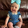 baby, child, smiling, blue_bow, headband, blue_overall, white_socks, frills, leather_couch, indoor, cute, happy, sitting, infant, portrait, clothing, hand, face, skin, person