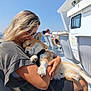 woman, dog, hugging, boat, outdoor, sunny, sea, blue_sky, glasses, shorts, chair, relaxing, pet, happy, leash, casual_clothing, daytime, people, vacation, nature
