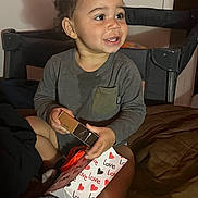 Bryan joined the competition — help win amazing prizes! toddler, child, curly_hair, smiling, gift_bag, love, hearts, box, bed, blanket, indoor, clothing, long_sleeve, sitting, person, happy, toy, present, room, cozy