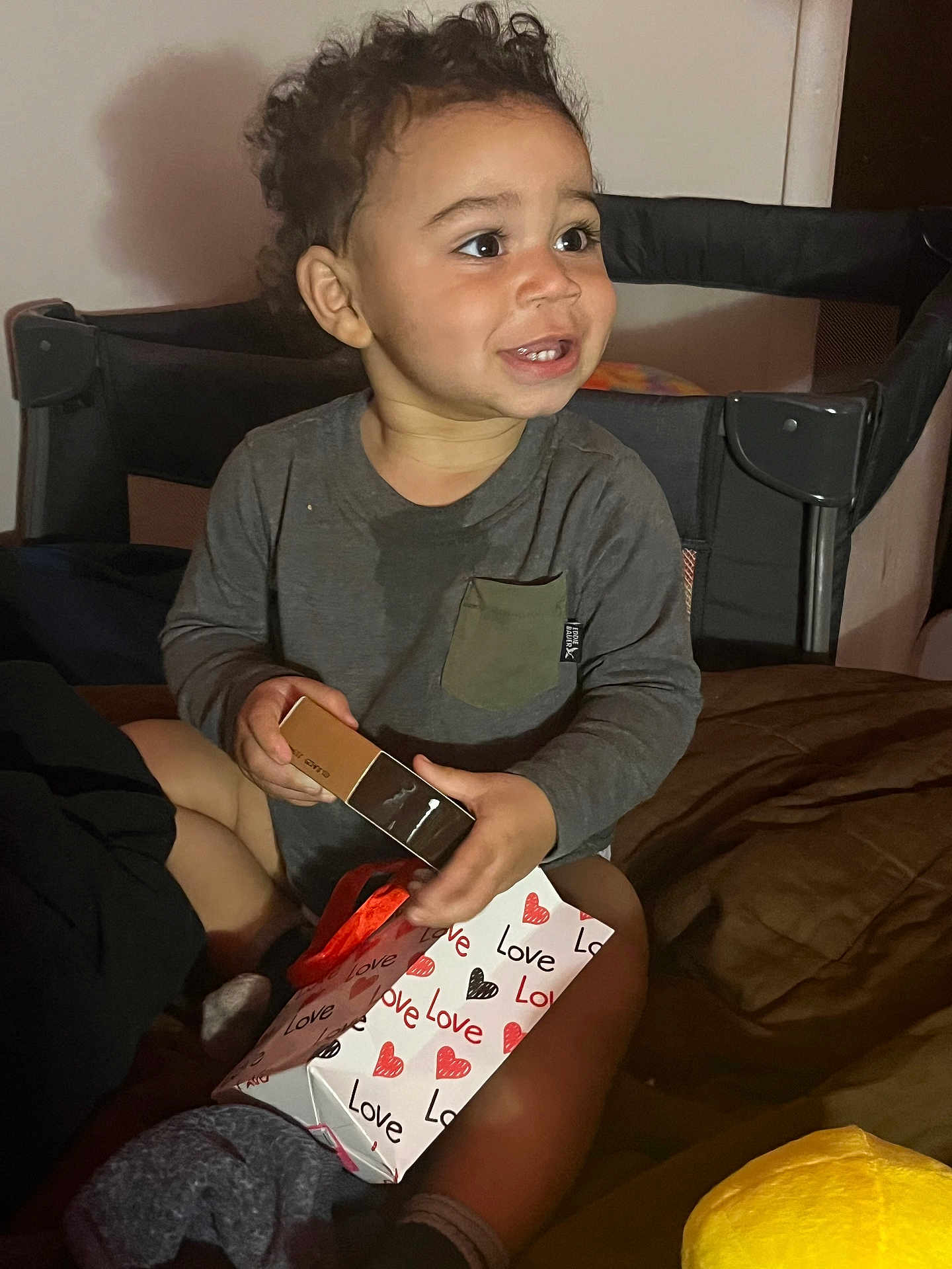 Bryan joined the competition — help win amazing prizes! toddler, child, curly_hair, smiling, gift_bag, love, hearts, box, bed, blanket, indoor, clothing, long_sleeve, sitting, person, happy, toy, present, room, cozy
