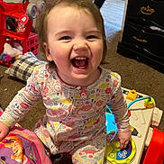 Olivia is registered to the contest to win money with this photo: toddler, child, smiling, laughing, pajamas, toy, playtime, indoor, carpet, furniture, dresser, colorful, educational_toy, happy, person, cute, young_child, room, playroom, joyful