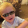 toddler, child, sunglasses, smile, indoor, carpet, toy, shirt, messy, furniture, couch, face, person, blond_hair, happy, young_child, reflection, casual, playtime, home