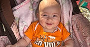Kensleigh is registered to the contest to win money with this photo: baby, smiling, orange_shirt, blanket, stroller, cozy, infant, child, cute, happy, soft_texture, indoor, portrait, clothing, head, face, person, baby_girl, baby_boy, toddler
