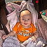 baby, smiling, orange_shirt, blanket, stroller, cozy, infant, child, cute, happy, soft_texture, indoor, portrait, clothing, head, face, person, baby_girl, baby_boy, toddler