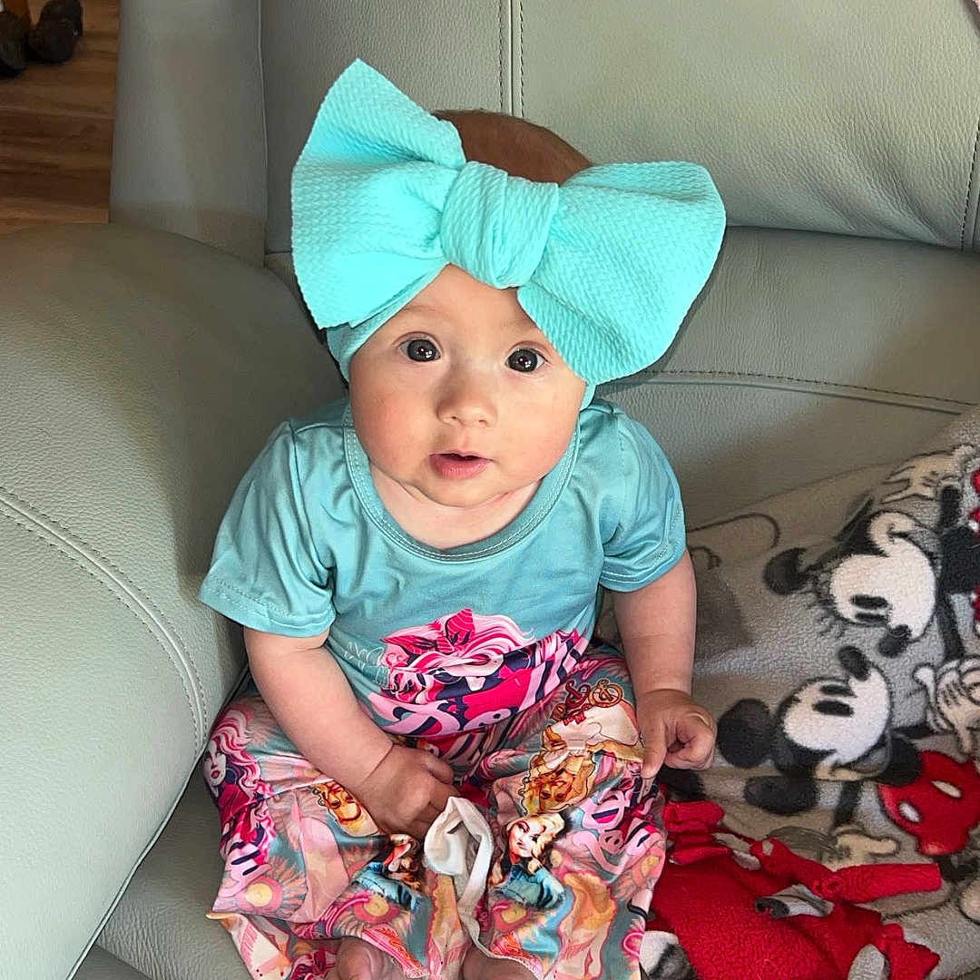 Kensleigh joined the competition — help win amazing prizes! baby, child, headband, bow, sitting, couch, leather, blanket, mickey_mouse, plush_toy, colorful_clothing, pants, blue_shirt, indoors, looking_up, wide_eyes, cute, infant, small_feet, home