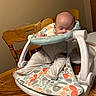 baby, infant, sleeping, baby_seat, wooden_table, wooden_chair, indoor, pajamas, colorful_pattern, face, head, hand, furniture, home, quiet, rest, comfort, child, person, nap