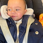 Hector a rejoint le concours — aidez-le/la à gagner de superbes lots ! toddler, child, baby, jacket, coat, car_seat, seatbelt, toy, orange, face, expression, curious, warm_clothing, indoor, closeup, person, portrait, smile, young, safety