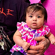 Elena is registered to the contest to win money with this photo: baby, child, person, hand, tattoo, clothing, dress, pattern, butterfly, pink, purple, adult, holding, curious, portrait, face, skin, indoor, closeup, cute