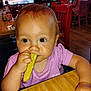 Larrea is registered to the contest to win money with this photo: baby, background_people, bright_eyes, casual, child, curious, dining, eating, face, food, furniture, hand, high_chair, indoor, person, pickle, purple_shirt, restaurant, table, wooden_table