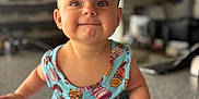 Kalani is registered to the contest to win money with this photo: baby, child, purple_bow, headband, colorful_dress, pastry_pattern, smiling, happy, indoor, countertop, baby_wipes, sitting, cute, portrait, face, human, infant, playful, clothing, closeup