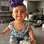 baby, child, purple_bow, headband, colorful_dress, pastry_pattern, smiling, happy, indoor, countertop, baby_wipes, sitting, cute, portrait, face, human, infant, playful, clothing, closeup
