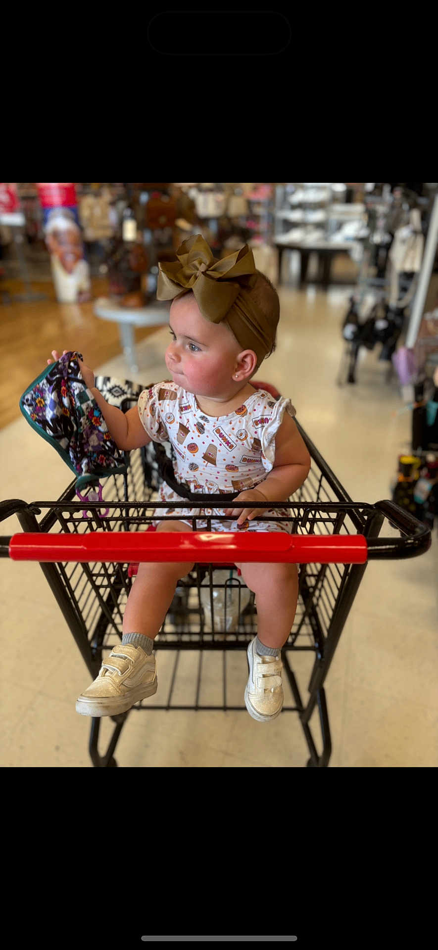 Kalani is registered to the contest to win money with this photo: toddler, child, shopping_cart, headband, bow, mask, shoes, socks, store, indoor, floor, clothing, person, baby, cute, curious, seat, shopping, retail, casual