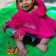 Mila participe au concours pour gagner de l'argent avec cette photo : baby, child, smiling, pink_towel, hooded_towel, green_mat, outdoor, toy, bead_maze, soda_bottle, hand, smile, feet, grass, rocks, nature, playtime, cute, person, portrait