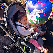 Mila a rejoint le concours — aidez-le/la à gagner de superbes lots ! balloon, casual, chairs, child, cozy_clothing, crepes, family, heart_shaped, man, outdoor, pavement, pink_bow, playful, shoes, sign, stroller, sunlight, table, toddler, unicorn