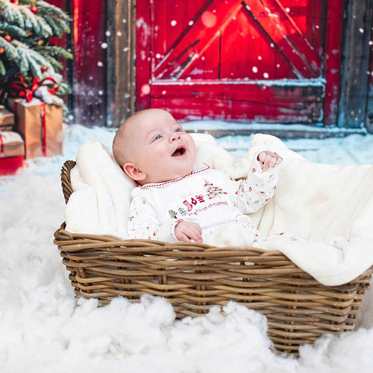 Kayden Lee is registered to the contest to win money with this photo: baby, basket, blanket, christmas, christmas_tree, decorations, door, festive, floor, furniture, gift, holiday, indoors, joyful, pajamas, person, portrait, smiling, snow, winter