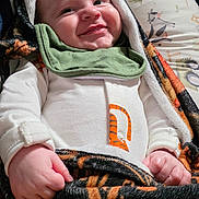 Jasper is registered to the contest to win money with this photo: animal_print, baby, blanket, child, clothing, cozy, cute, face, green_bib, hand, happy, indoor, infant, lying_down, newborn, pillow, portrait, smiling, soft_texture, tiger_stripe