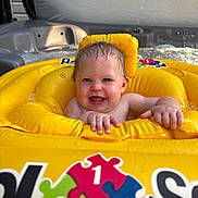 Summer is registered to the contest to win money with this photo: baby, child, inflatable, yellow, water, pool, smiling, happy, wet_hair, sitting, hot_tub, face, skin, hands, blue_eyes, toy, colorful, indoor, water_bubbles, playful