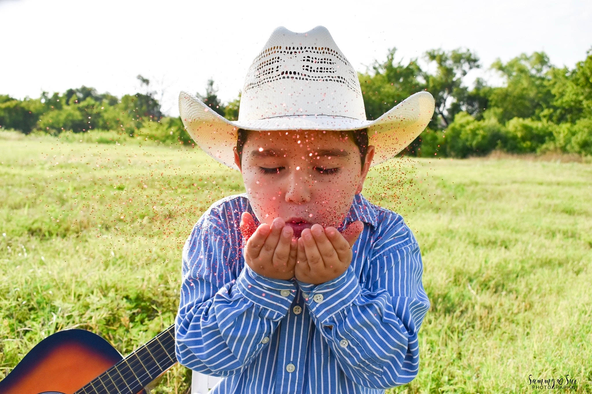 Braiden joined the competition — help win amazing prizes! cowboy, cowboy_hat, farm, fashion_accessory, field, grass, grassland, guitar, hat, headgear, headwear, person, plucked_string_instruments, rural_area, sun_hat, ukulele