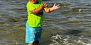 Jeremiyahh is registered to the contest to win money with this photo: child, toddler, water, sea, ocean, splashing, wet_hair, bright_clothing, neon_shirt, blue_shorts, palm_tree_pattern, happy, smiling, summer, outdoor, sunlight, waves, playful, fun, vacation