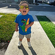 Jeremiyahh joined the competition — help win amazing prizes! toddler, child, sunglasses, blue_tshirt, dinosaur_graphic, shorts, white_shoes, sidewalk, shadow, grass, suburban, house, car, sunlight, happy, smiling, outdoor, daytime, person, curly_hair