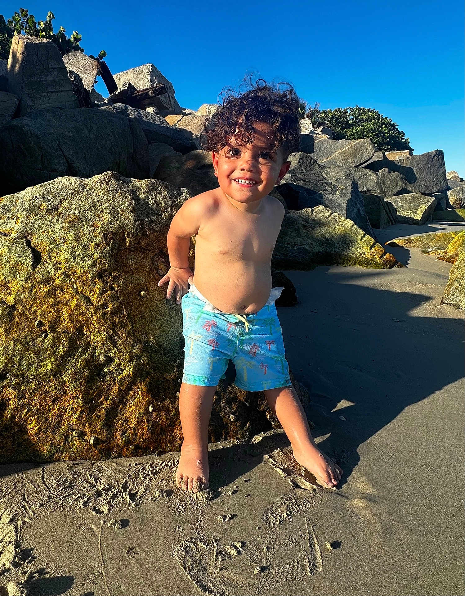Jeremiyahh is registered to the contest to win money with this photo: child, boy, beach, sand, rock, sunlight, shadow, curly_hair, barefoot, smiling, outdoor, nature, summer, toddler, playful, coast, vacation, water, sky, casual_clothing