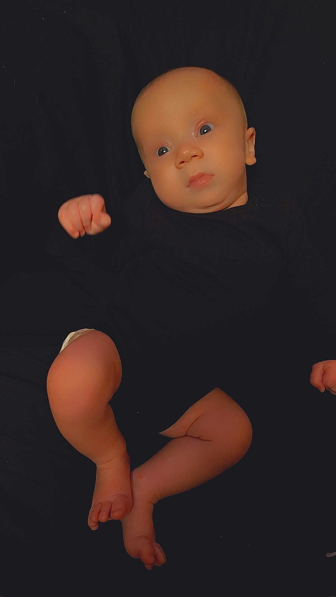 Xavion is registered to the contest to win money with this photo: baby, infant, newborn, child, portrait, lying_down, black_background, onesie, bare_legs, feet, hands, eyes, face, skin, closeup, cozy, looking_up, candid, soft_lighting, studio_style