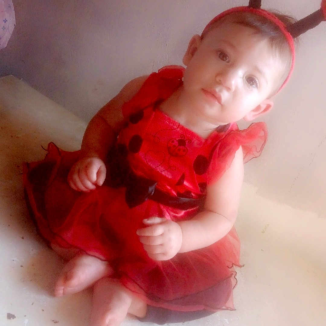 Jazmine is registered to the contest to win money with this photo: antennae, baby, barefoot, child, costume, curious, cute, floor, headband, indoors, ladybug_costume, light_skin, playful, portrait, red_dress, short_hair, sitting, toddler, wall, young_child