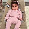 baby, child, pink_outfit, hair_bow, baby_seat, indoor, carpet, wooden_floor, curious_expression, cozy_clothing, wide_eyes, wild_hair, footwear, plush_socks, home_interior, furniture, decor, portrait, sitting, infant