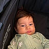 baby, child, infant, face, person, clothing, onesie, flower_pattern, dark_hair, stroller, car_seat, cozy, cute, portrait, young_child, indoors, soft_texture, sleepy, hand, closeup