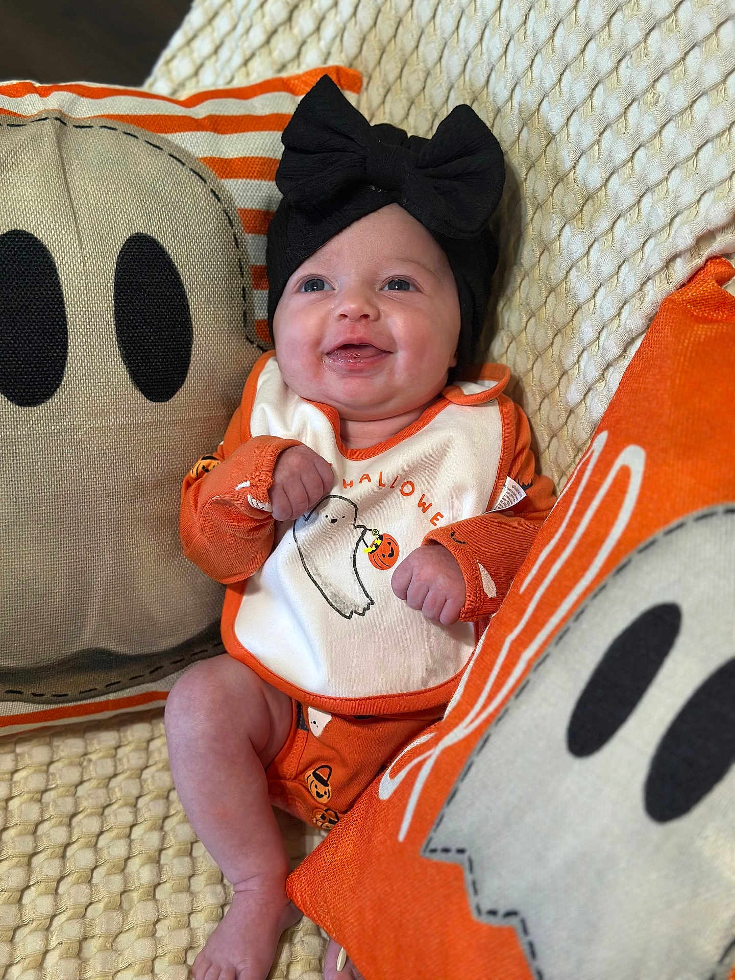 Brayleigh is registered to the contest to win money with this photo: baby, infant, smiling, black_bow, orange_clothing, halloween, ghost_pillow, decorative_pillow, blanket, couch, happy, cute, indoor, portrait, child, headwear, holiday, festive, infant_clothing, cozy