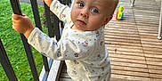 Elio a rejoint le concours — aidez-le/la à gagner de superbes lots ! toddler, child, baby, pajamas, blue_eyes, balcony, wooden_floor, toy, high_chair, outdoor, curious, standing, handrail, footwear, person, infant, daylight, expression, clothing, play