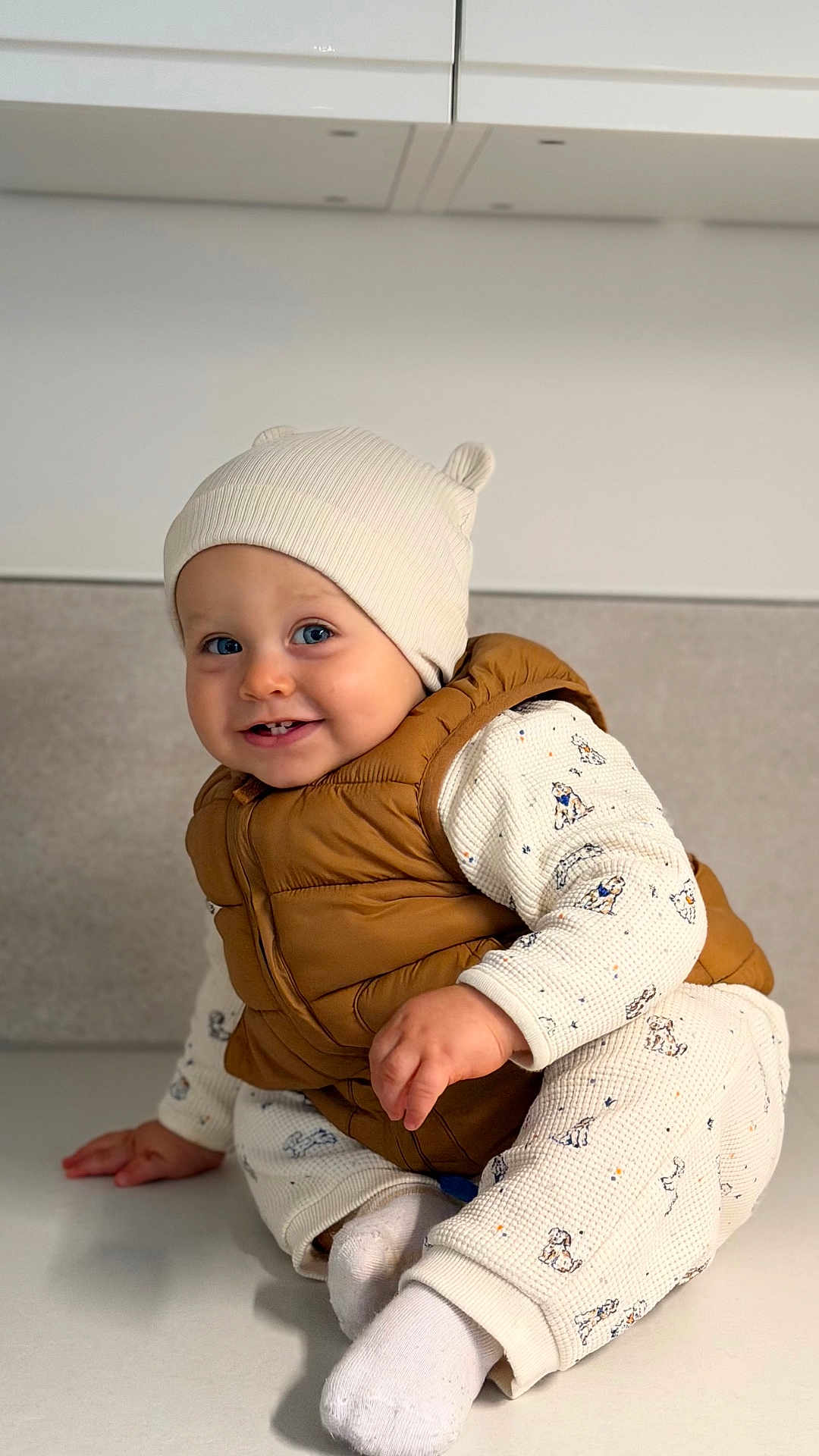 Elio participe au concours pour gagner de l'argent avec cette photo : baby, child, smiling, hat, vest, white_socks, indoor, cute, infant, clothing, face, person, sitting, happy, portrait, warm_clothes, baby_girl, baby_boy, floor, background