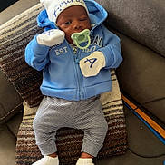 Amirion is registered to the contest to win money with this photo: baby, infant, pacifier, blue_hoodie, mittens, striped_pants, white_socks, couch, pillow, indoor, child, cute, relaxed, face, hat, looking, seated, home, soft_lighting, young