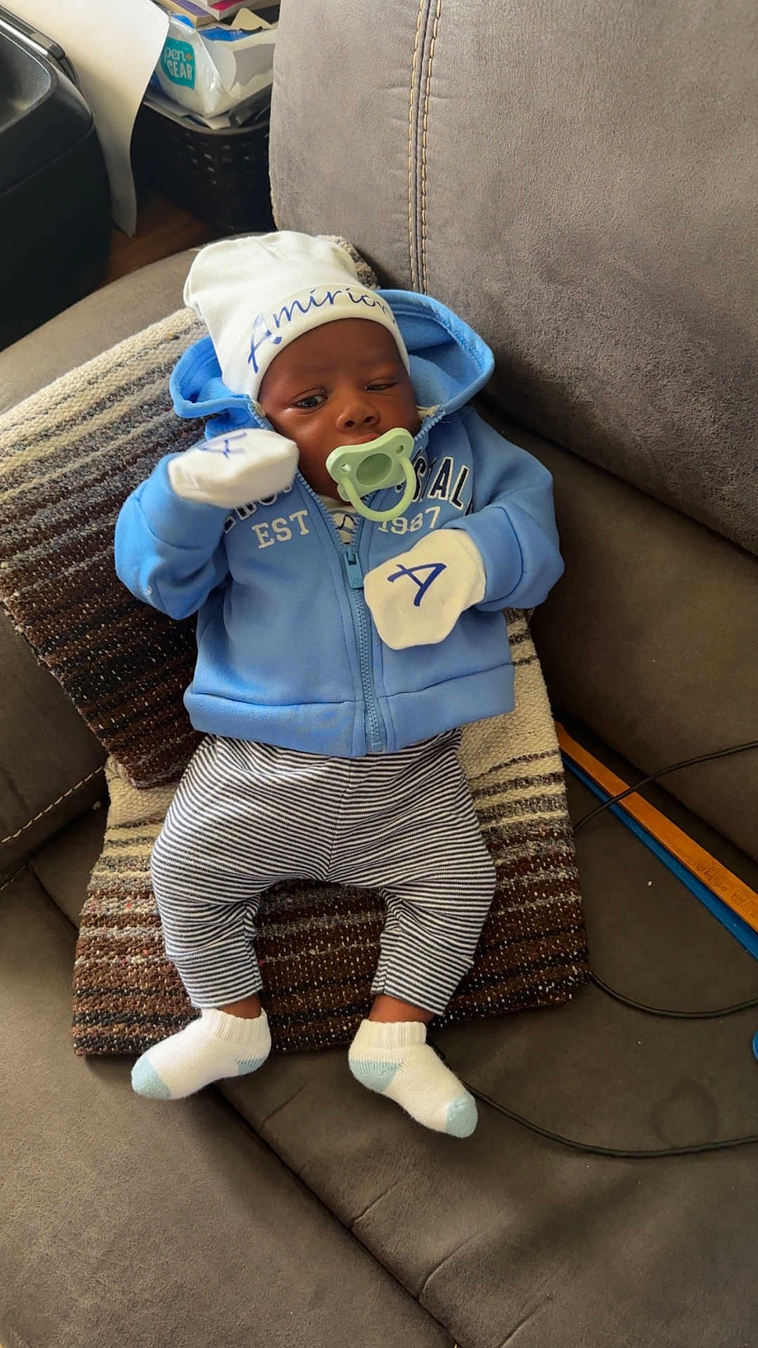 Amirion is registered to the contest to win money with this photo: baby, infant, pacifier, blue_hoodie, mittens, striped_pants, white_socks, couch, pillow, indoor, child, cute, relaxed, face, hat, looking, seated, home, soft_lighting, young