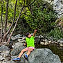 Andrew Matteo Romero is registered to the contest to win money with this photo: child, rock, creek, trees, greenery, nature, outdoor, water, shorts, tshirt, pointing, footwear, rocks, forest, daylight, person, sitting, casual, landscape, adventure
