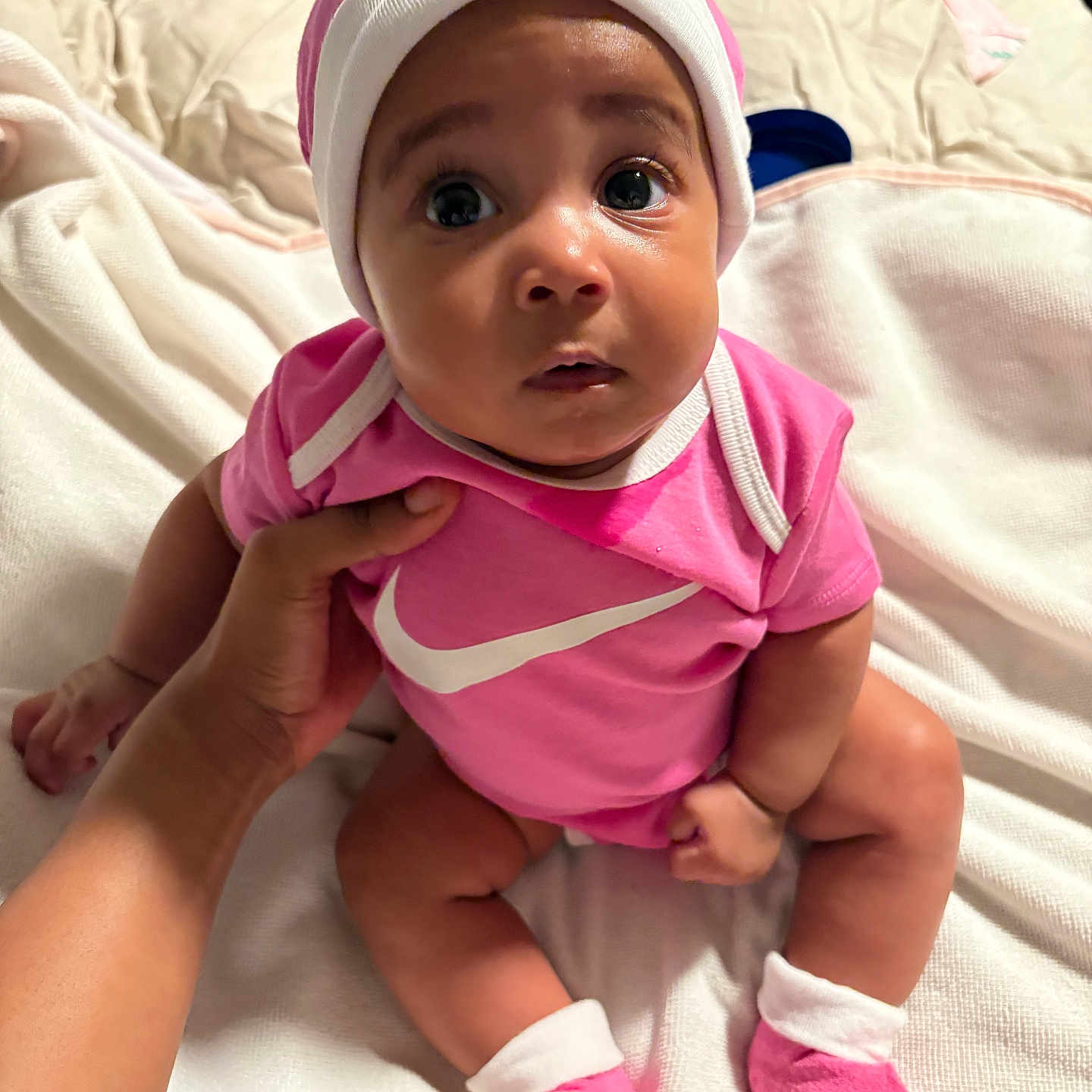 Rumani joined the competition — help win amazing prizes! baby, bed, blanket, child, close_up, curious_expression, cute, hand, hat, indoor, infant, nike_logo, person, pink_clothing, portrait, sitting, socks, soft_lighting, supporting_hand, wide_eyes